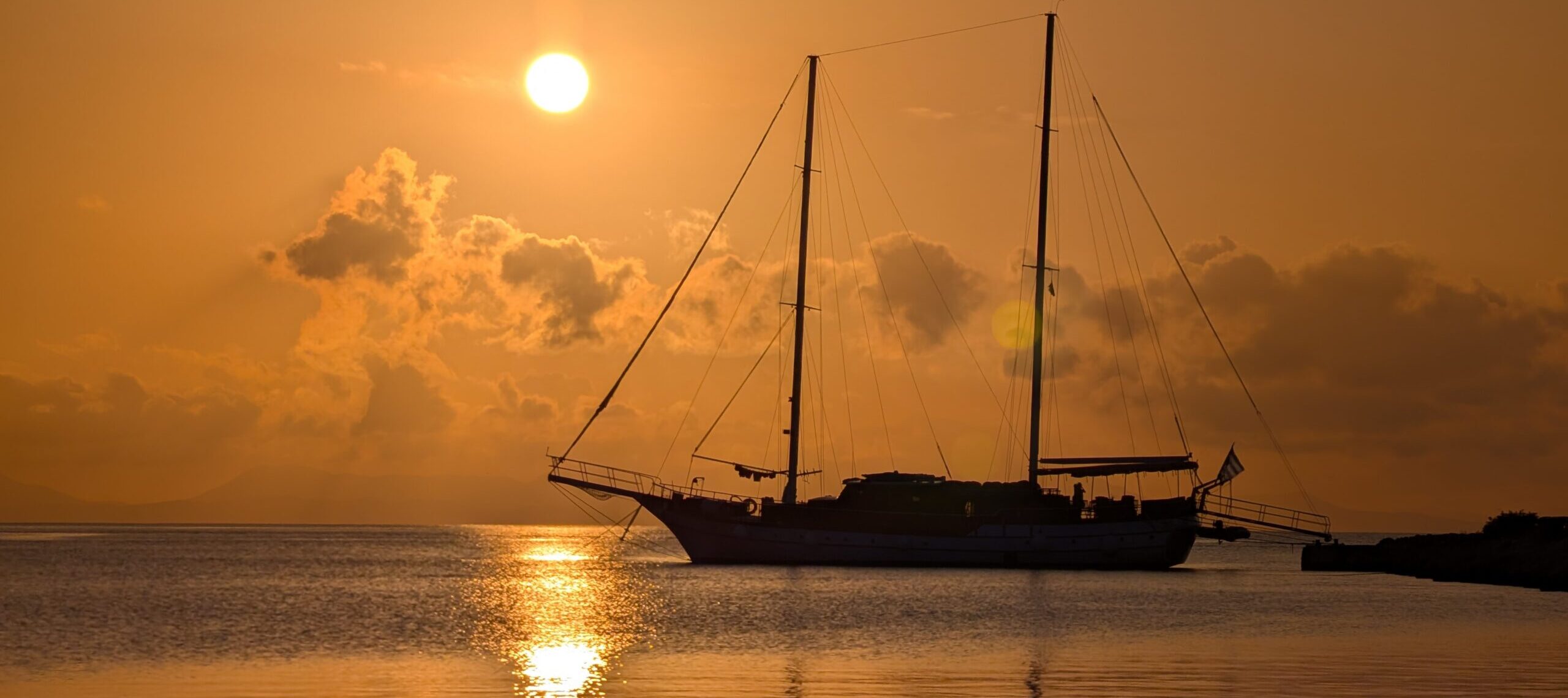 Two-mast sailing boat in front of setting sun