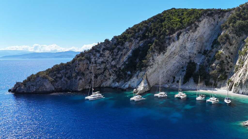 island with beach and sailing boats and catamarans achored in front