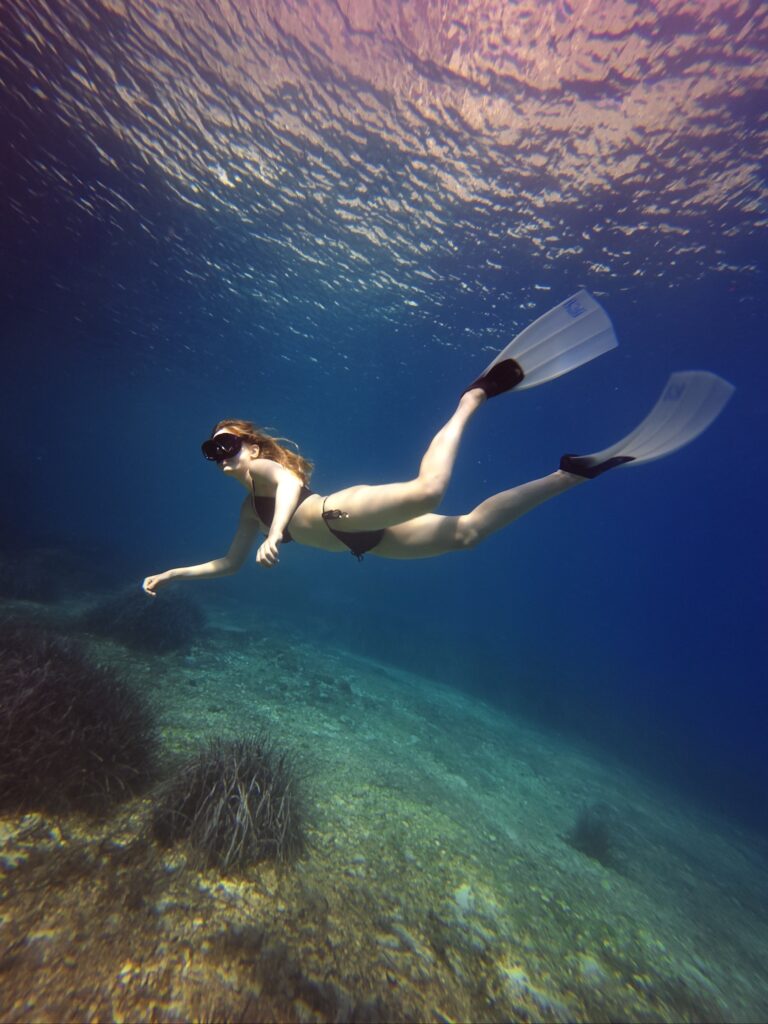 lady with mask and fins underwater snorkeling over ocean ground with seagrass