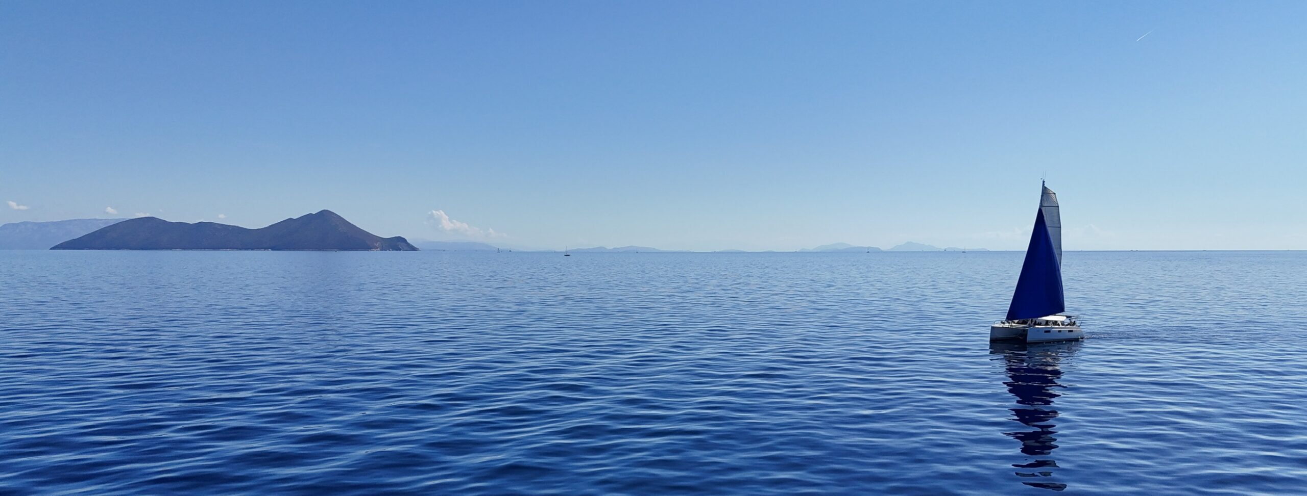 sailing catamaran under sail in front of Atokos island